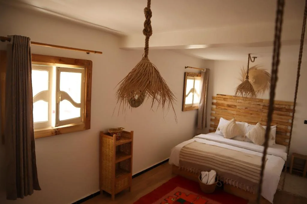 Double bedroom at Grip Sea Morocco in Anza with a wooden bed, woven pendant lamps and a bright window