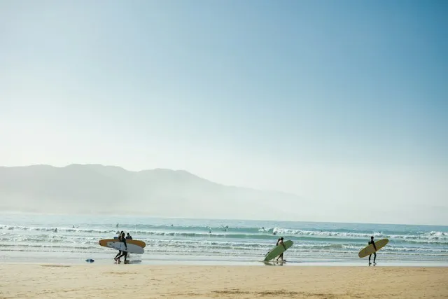 Surfers walking to the water with longboards along the mellow sand bottom of Imsouane Bay