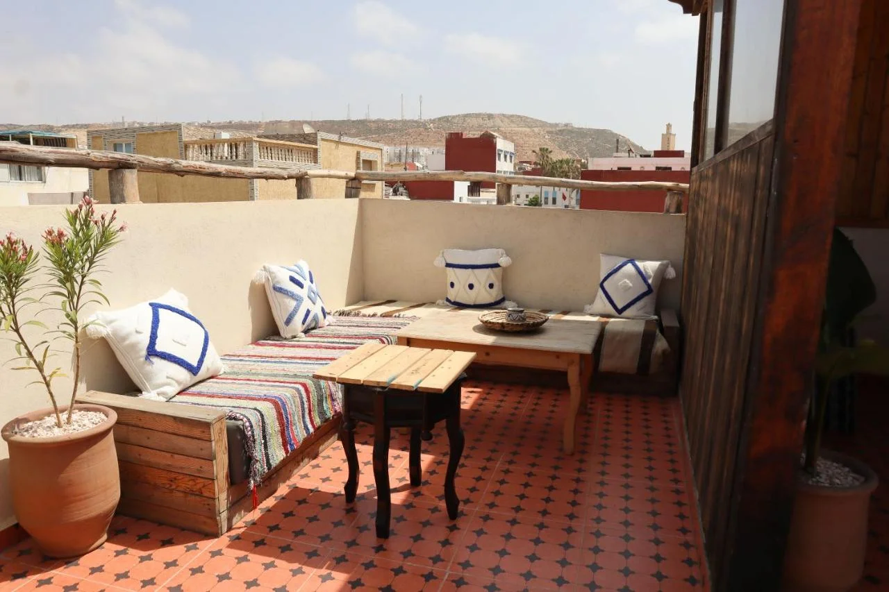 Sunlit rooftop terrace at Grip Sea Morocco in Anza, with cushioned seating, wooden tables and patterned tiles